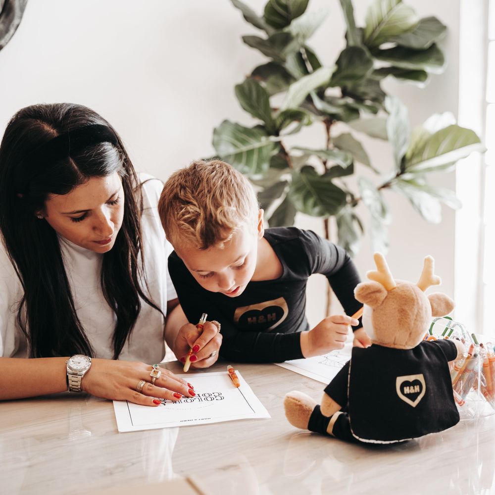 Mom and two children sitting at a table with a plush Hartie the Power Pal, coloring.